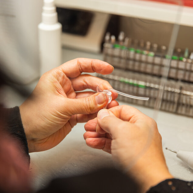 Die Hände einer Mitarbeiterin welche ein Hörgerät reparieren