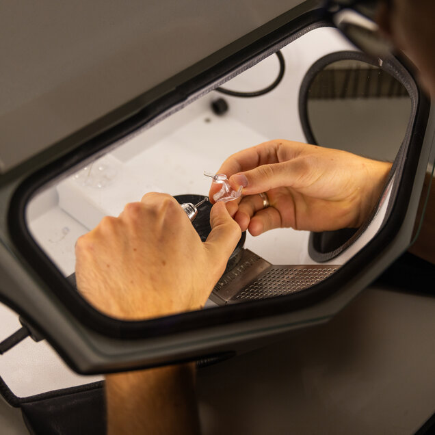 Die Hände einer Mitarbeiterin beim Zusammenbau eines Hörgerätes